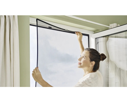 Une femme installe une moustiquaire sur une fenêtre.