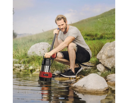 Un homme est accroupi au bord d''une étendue d''eau et tient une pompe à eau sale.