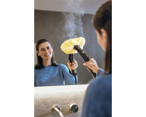 Frau verwendet einen Dampfreiniger mit gelbem Tuchaufsatz an einem Spiegel im Badezimmer