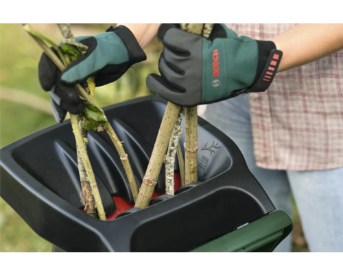 Deux mains gantées remplissent un broyeur de branches.