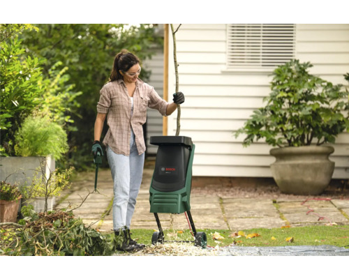 Une femme utilise un broyeur de branches dans le jardin avec des outils de jardinage et des déchets de jardin