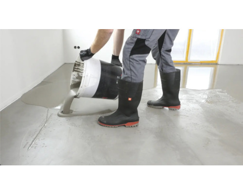 Estrich gießen: Mann schüttet Estrich aus Eimer auf Boden.