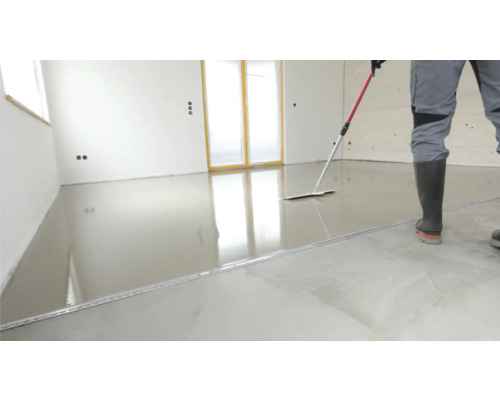 Ein Mann verteilt Ausgleichsmasse auf einem Boden mit einem Rakel.