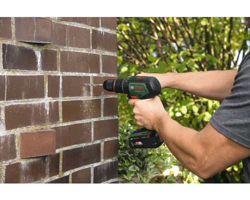 Un homme perce un trou dans un mur de briques avec une perceuse-visseuse sans fil