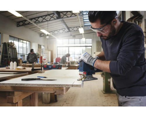 Homme coupant une plaque de bois avec une scie sauteuse dans un atelier