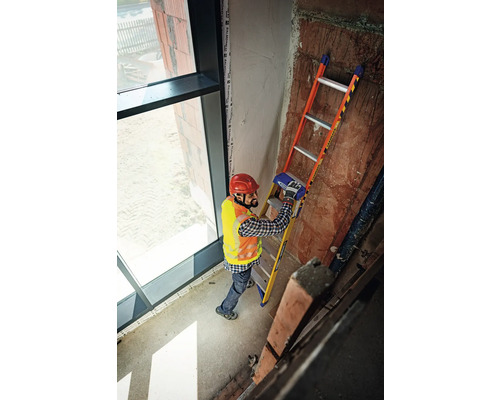 Ein Mann mit Helm und Sicherheitsweste steht auf einer Leiter in einem Gebäude.