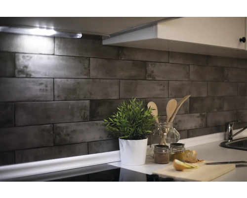 Scène de cuisine avec carrelage mural aspect pierre, plante et ustensiles de cuisine sur le plan de travail.
