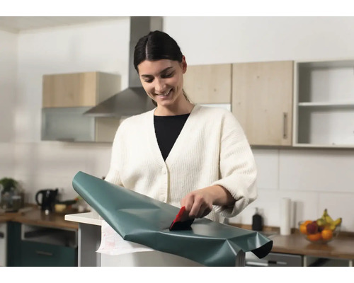 Une femme applique un film décoratif avec une raclette dans la cuisine