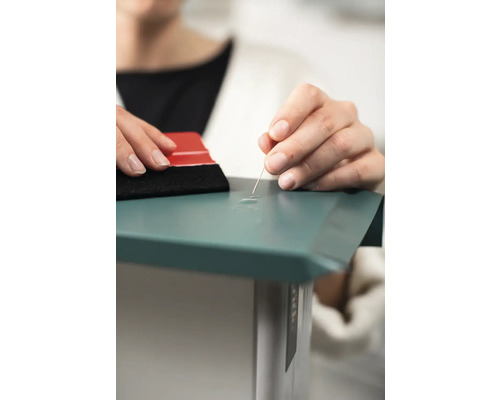 Person entfernt Luftblasen aus einer Folie mit einer Nadel und einem Rakel.