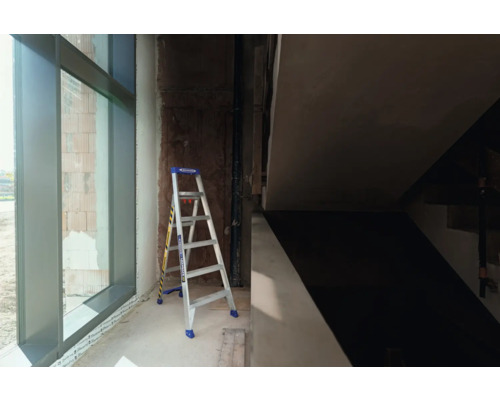 Eine Stehleiter steht in einem Rohbau neben einem Fenster.