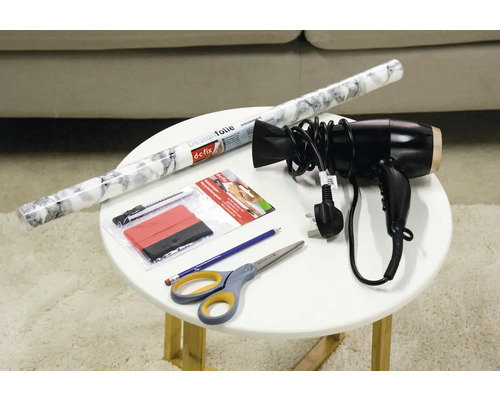 Dekorfolie, Rakel, Cutter, Schere, Bleistift und Fön auf einem Tisch