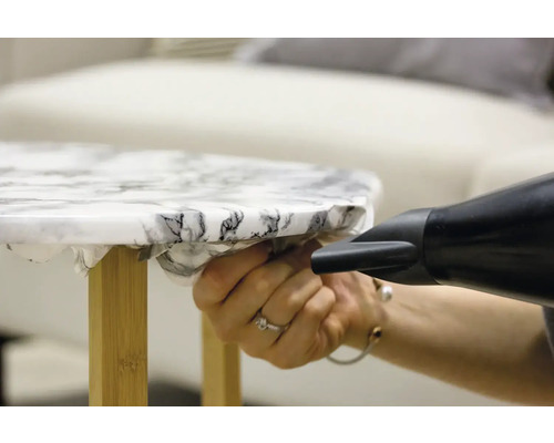 Anbringen einer selbstklebenden Folie auf einem Tisch mit einem Heißluftfön