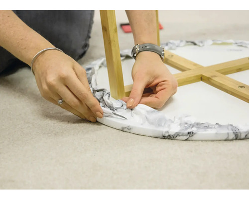 Eine Person schneidet die Verpackung von einem runden Tisch mit Holzbeinen.