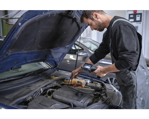 Un mécanicien inspecte le compartiment moteur d'une voiture avec une caméra d'inspection.
