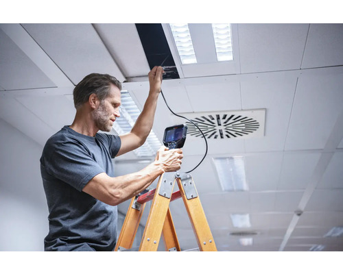 Un homme inspecte un plafond avec une caméra d'inspection depuis une échelle