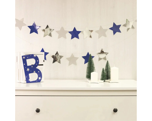 Dekorative Szene mit Sternengirlande, Dekobuchstabe, Weihnachtsbäumen und Kerzen auf einer Kommode