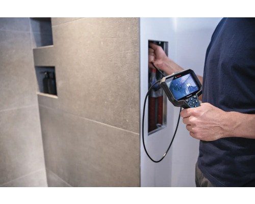 Un homme utilise une caméra d'inspection Bosch pour examiner des tuyaux dans un mur.