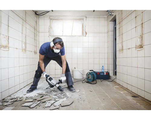 Homme avec un marteau pneumatique effectuant des travaux de rénovation dans une pièce carrelée au mur et au sol