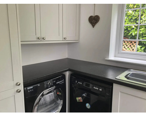Buanderie lumineuse avec lave-linge, sèche-linge, lave-vaisselle, plan de travail et armoire murale