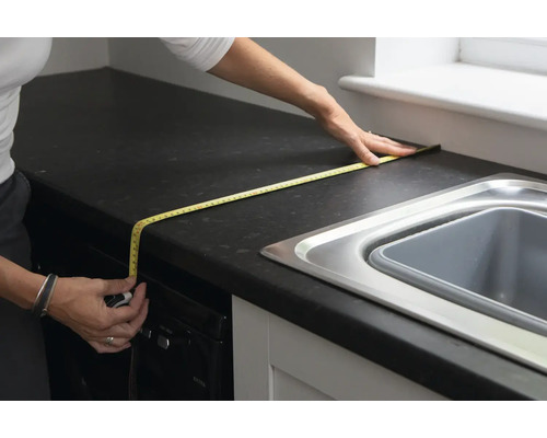 Une personne mesure un comptoir de cuisine avec un mètre ruban.