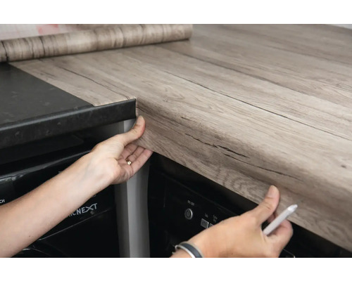 Scène de cuisine avec une personne appliquant un film autocollant sur un plan de travail.