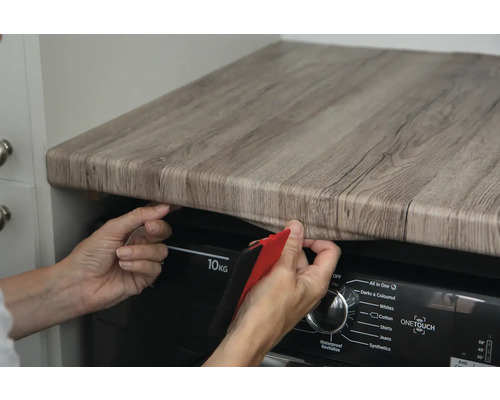 Une personne pose un film décoratif imitation bois sur un plan de travail.