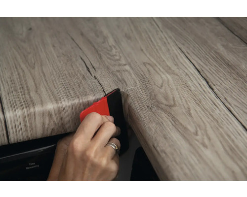 Une personne applique un film décoratif sur une surface avec une raclette