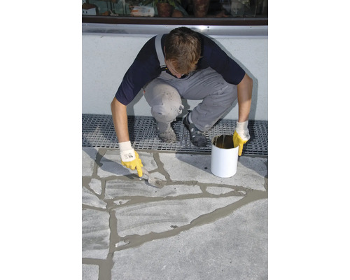 Ein Mann füllt mit einer Spachtel Fugen auf einer Betonoberfläche.