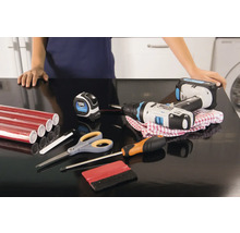 Surface de travail avec film de meuble rouge, visseuse sans fil, mètre ruban, tournevis, ciseaux et racloir pour la pose