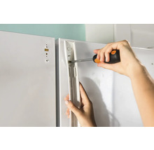 Une personne fixe un support sur une surface blanche à l''aide d''un tournevis.