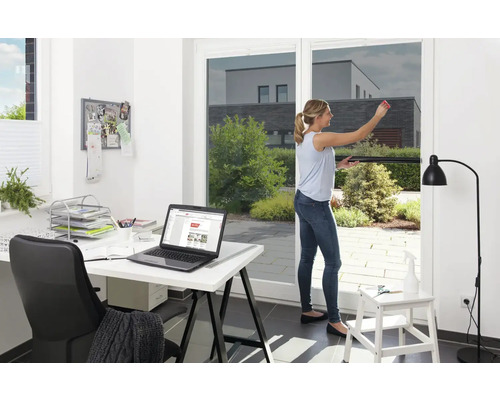 Frau bringt Sonnenschutzfolie an Fenster an, Büro im Hintergrund