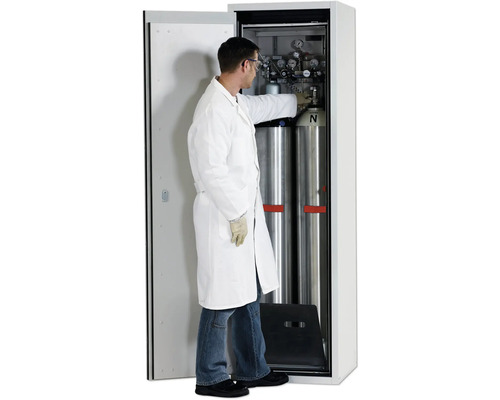 Un homme en tenue de laboratoire travaille sur des bouteilles de gaz comprimé dans une armoire de sécurité.