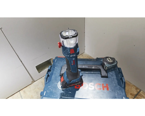 Bosch Logo. Akku-Baustrahler auf Werkzeugkoffer mit Messband vor Gipskartonwand