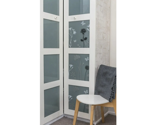 Weißer Schrank mit floralen Motiven und Glasfronten neben einem Stuhl mit einer grauen Decke