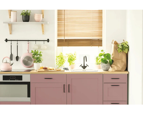 Cuisine lumineuse avec armoires roses, plan de travail en bois et ustensiles de cuisine