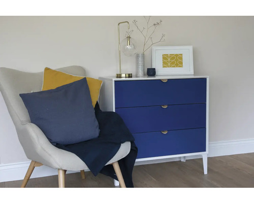 Scène de salon avec fauteuil, coussins, jeté de lit et commode avec lampe et articles de décoration