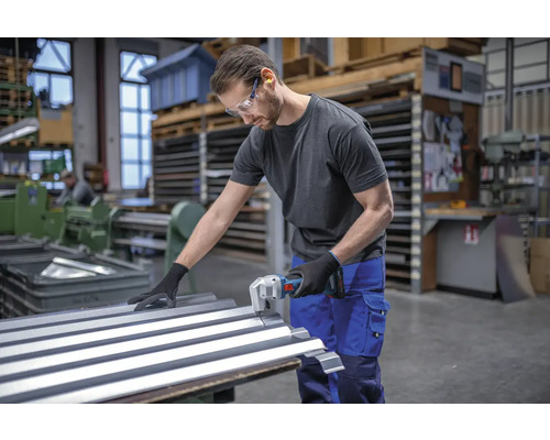 Un homme coupe de la tôle ondulée avec une grignoteuse dans un atelier.