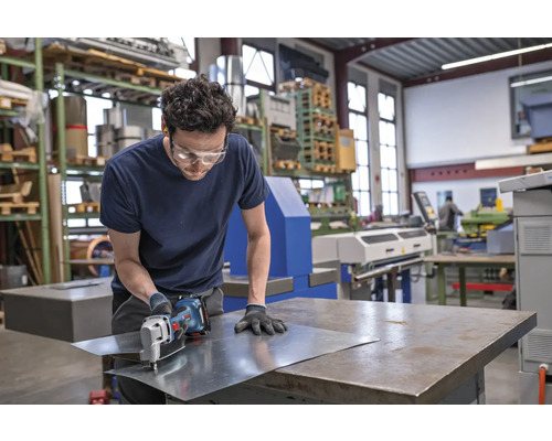 Artisan coupant une tôle avec une cisaille à tôle dans un atelier.