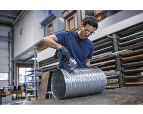 Un homme coupe un tuyau de ventilation en métal avec une grignoteuse.
