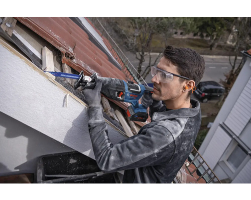 Un homme travaille avec une scie sabre sur un toit