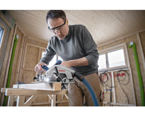 Un homme coupe du bois avec une scie circulaire portative Bosch dans un bâtiment en construction
