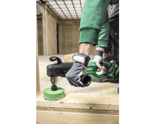 Eine Person bohrt mit einer Kernbohrmaschine ein Loch in ein Holzbrett. Marke HiKoki.