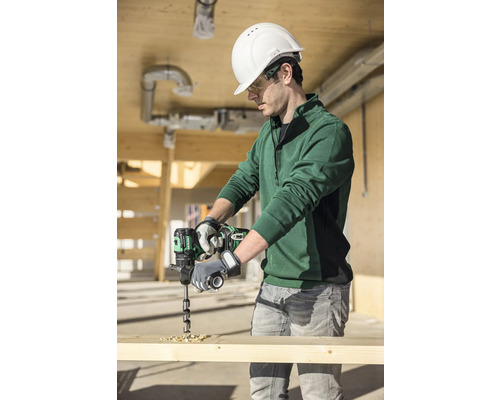 Ein Mann mit Schutzhelm und Schutzbrille bohrt mit einem Akkubohrer in ein Holzbrett.