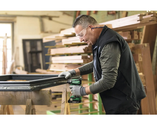 Un artisan assemble une fenêtre sur un établi à l''aide d''une visseuse sans fil.