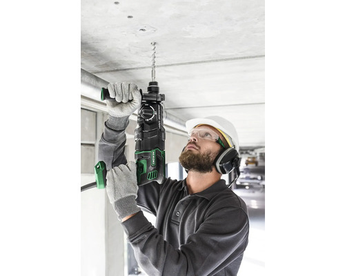 Un homme perce un trou dans un plafond en béton avec un perforateur.