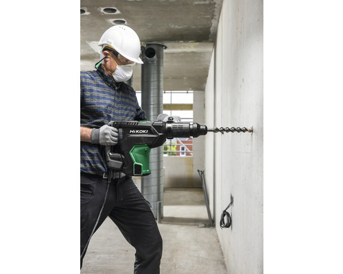 Un homme perce un trou dans un mur en béton avec un perforateur de la marque HiKOKI.
