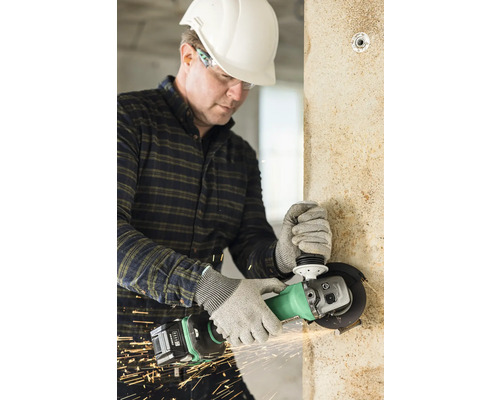 Artisan avec casque de protection et lunettes de protection travaillant un mur avec une meuleuse d''angle, produisant des étincelles.