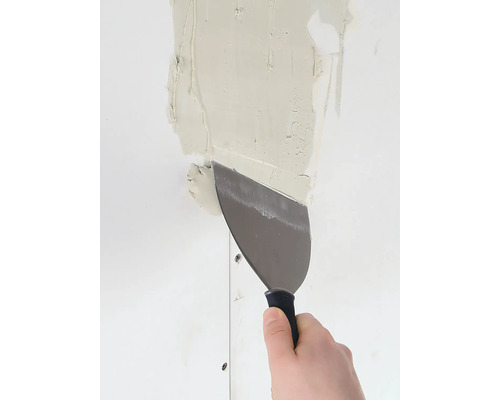 Une main lisse du plâtre sur un mur avec une spatule.