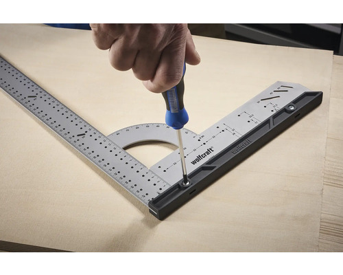 Logo Wolfcraft. Une personne fixe un angle multifonctionnel sur une plaque de bois avec un tournevis.