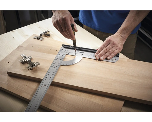 Eine Person verwendet ein Winkelmessgerät und einen Stift, um Markierungen auf einem Holzbrett neben Scharnieren zu machen.